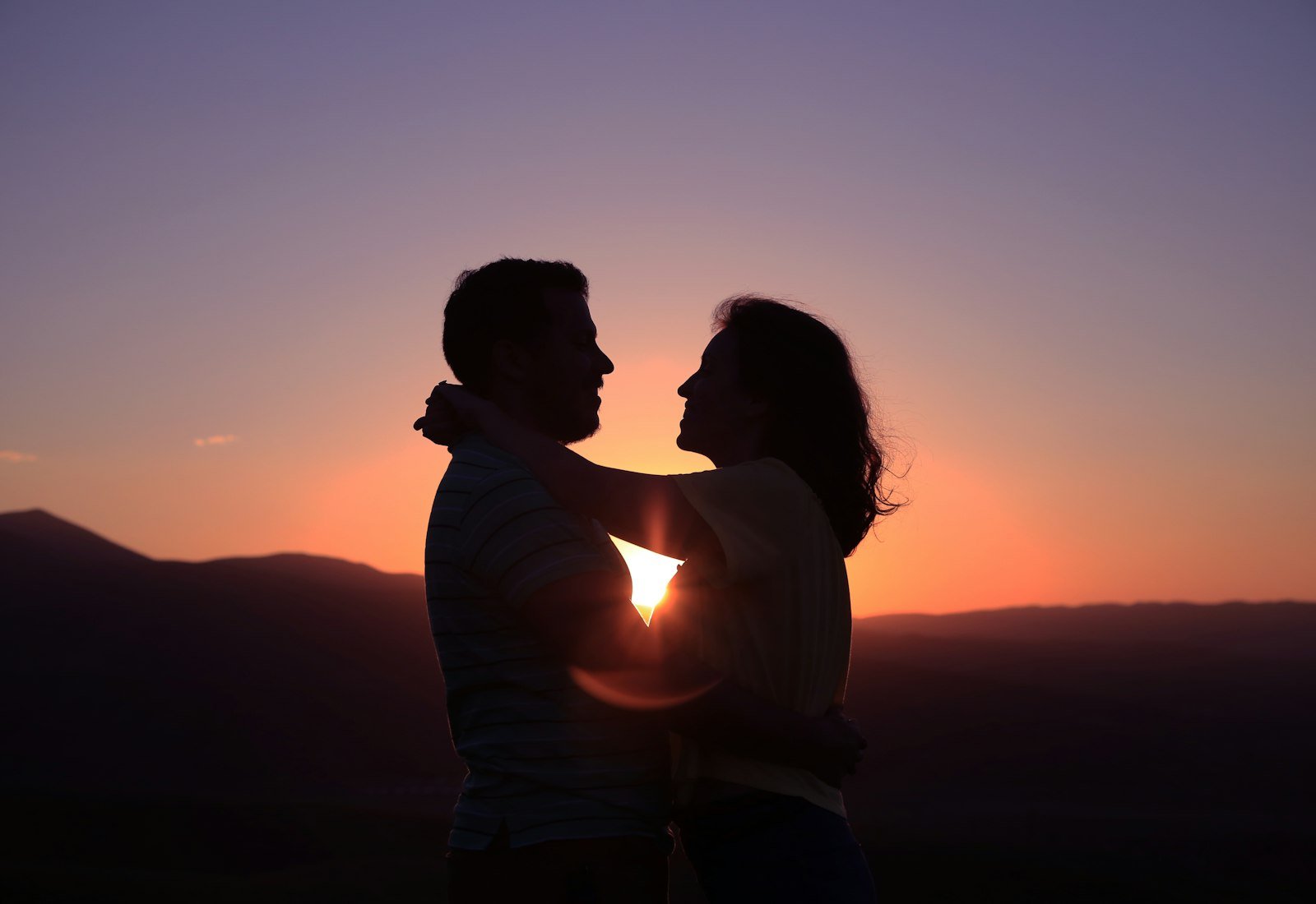 Casal em silhueta abraçado ao pôr do sol