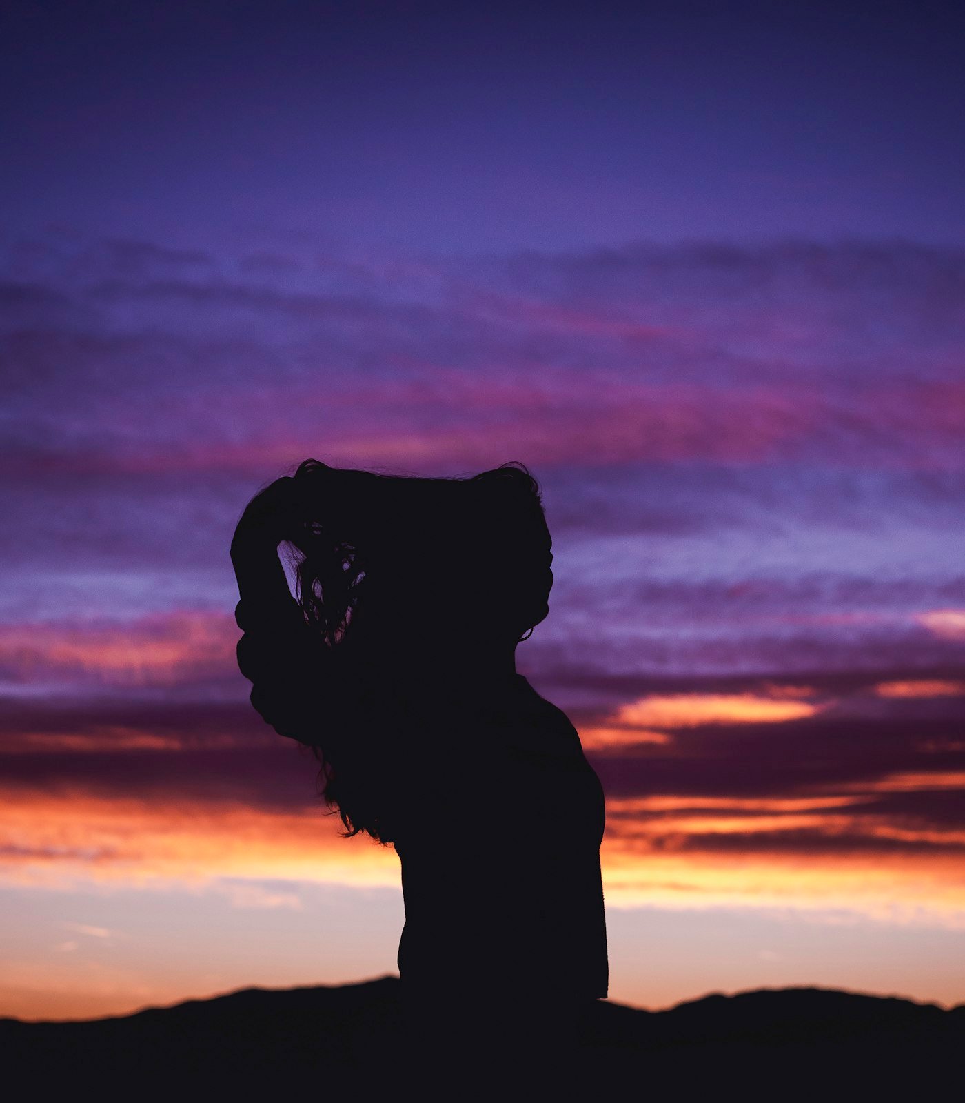 Silhueta de mulher diante de um céu roxo ao entardecer